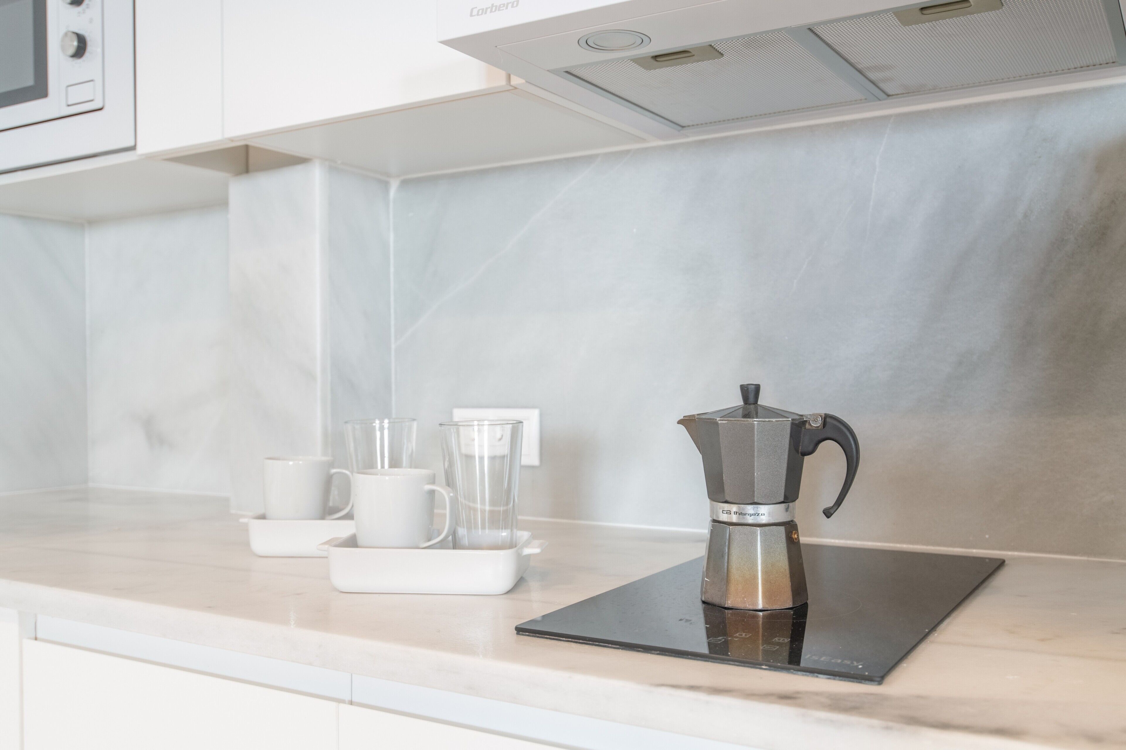 Cozinha com cafeteira, micro-ondas e jarra de café sobre um tapete preto.