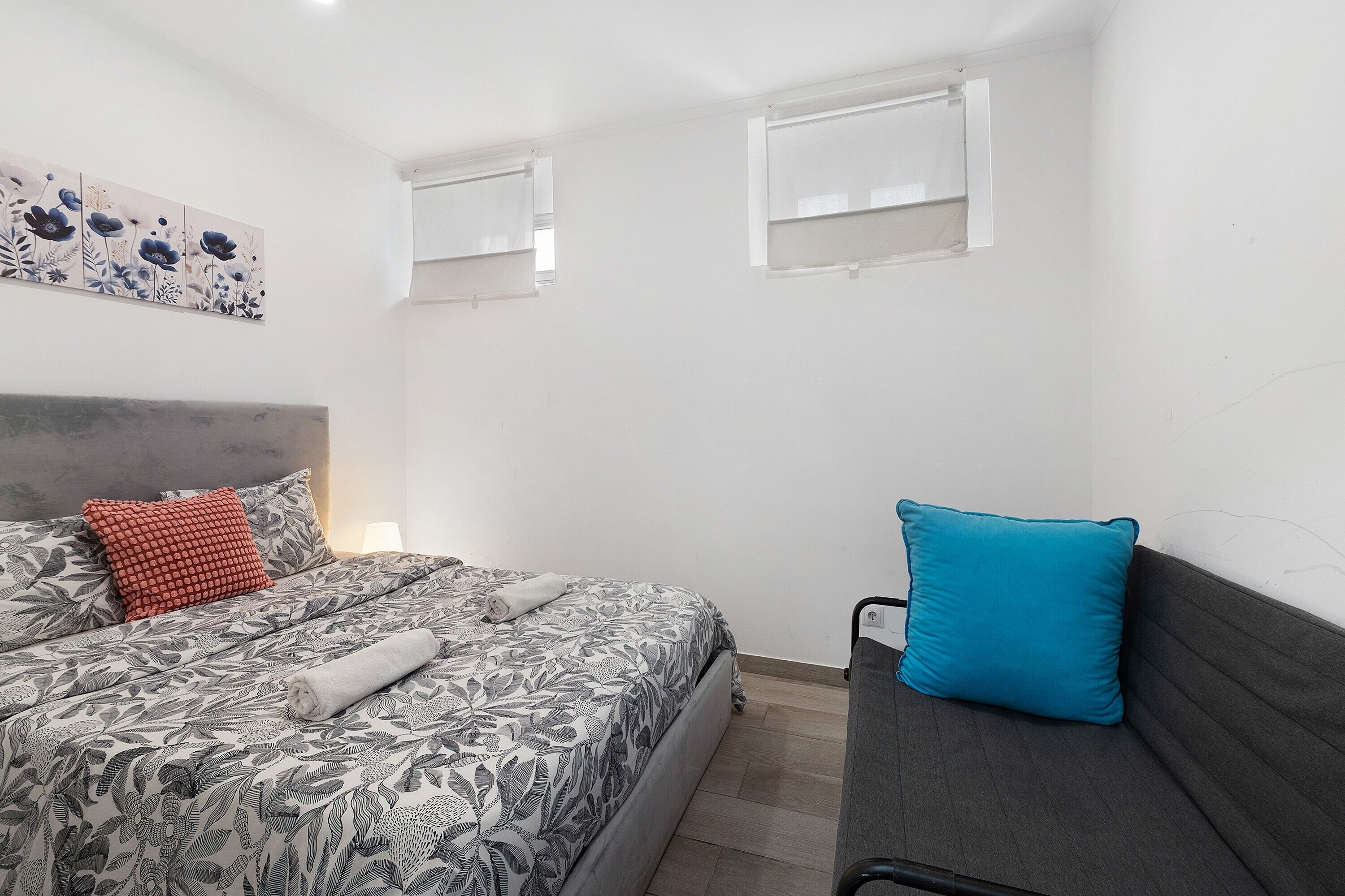 A bedroom with a bed, a sofa, a headboard, and two windows.