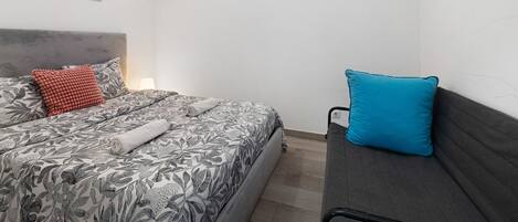 A bedroom with a bed, a sofa, a headboard, and two windows.