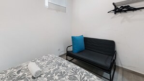 A small, sparsely furnished room with a bed, a sofa, a window, and a wall-mounted rack. - Lisbon Apartment – Excellent Central Location (Lisbon)