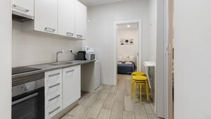 A modern kitchen with white cabinets, a built-in oven, and a microwave. There are two yellow stools near the kitchen counter. - Lisbon Apartment – Excellent Central Location (Lisbon)
