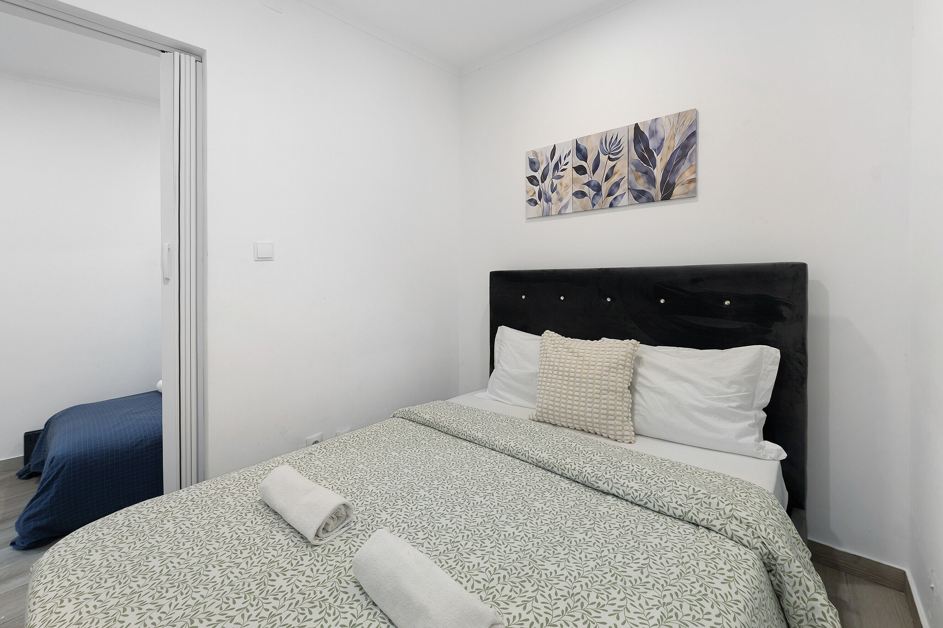 Un dormitorio con cama, cabecera, una obra de arte colgada en la pared y una puerta.
