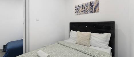 Un dormitorio con cama, cabecera, una obra de arte colgada en la pared y una puerta.