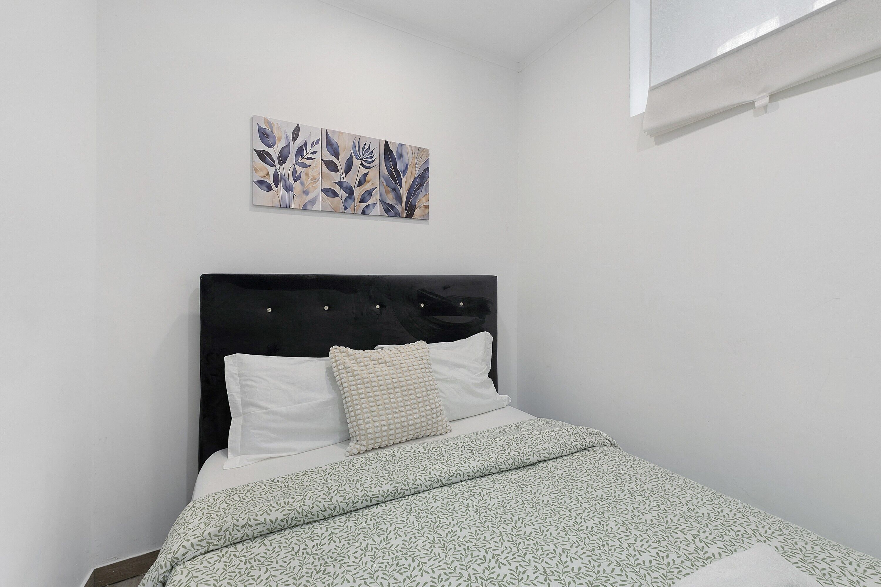A bed with a patterned bedspread, a headboard, and a wall-mounted artwork.