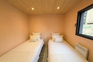 Una habitación pequeña y acogedora con dos camas individuales, una ventana y techo de madera.