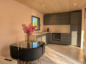 A modern kitchen with dark cabinets, a round glass table, and a vase of pink flowers. - Gîte2 neuf 2CH avec piscine privée - Calm, nature & comfort 10min from Bergerac (Lembras)