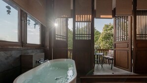 A bathroom with a freestanding bathtub, a window, and a door leading to an outdoor seating area. - Cloudland Skystream View Designer Inn (Lijiang)