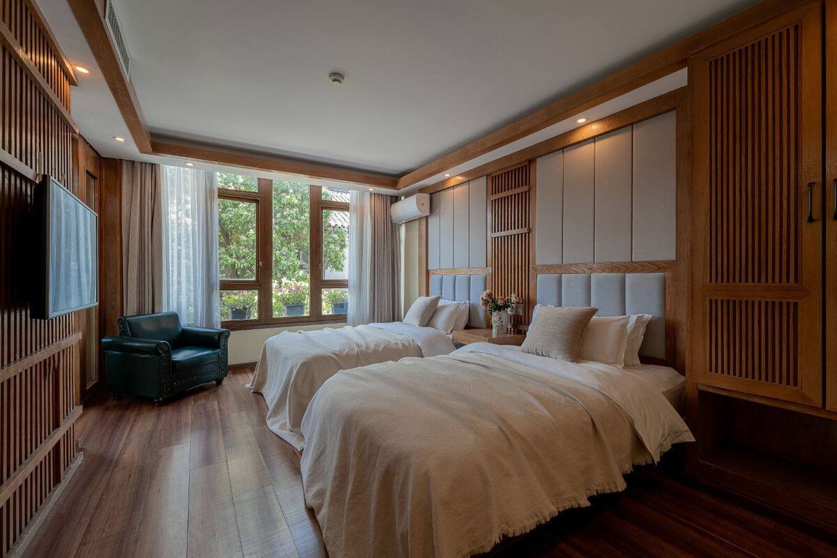 A bedroom with two beds, a TV, a chair, and large windows.