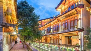 A traditional wooden building with a narrow waterway in front, a tree, and a pedestrian walkway. - Cloudland Skystream View Designer Inn (Lijiang)