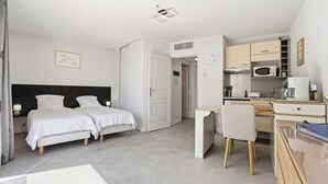 A bedroom with two beds, a desk, a chair, and a kitchenette. - Air-conditioned studio for 2 people, near the shops (Grasse)