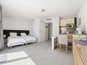 A bedroom with two beds, a desk, a chair, and a kitchenette. - Air-conditioned studio for 2 people, near the shops (Grasse)