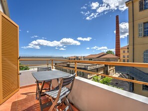 Un balcon avec une table et des chaises, donnant sur un bâtiment historique doté d’une haute cheminée.