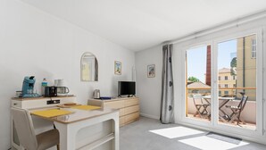A modern room with a desk, chair, coffee maker, TV, and a balcony with chairs. - Air-conditioned studio for 2 people, near the shops (Grasse)