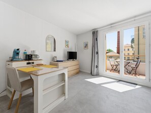 A modern room with a desk, chair, coffee maker, TV, and a balcony with chairs. - Air-conditioned studio for 2 people, near the shops (Grasse)