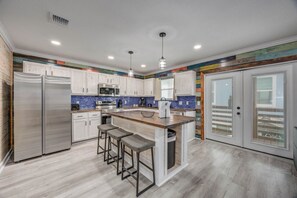 A modern kitchen with stainless steel appliances, a central island with stools, and a colorful backsplash. - CL3 Shared Pool, Charcoal Grill, Old Town Port A (Port Aransas)