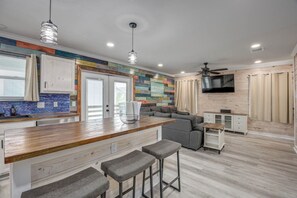 A modern kitchen with a wooden countertop, bar stools, a gray sofa, and a TV mounted on the wall. - CL3 Shared Pool, Charcoal Grill, Old Town Port A (Port Aransas)