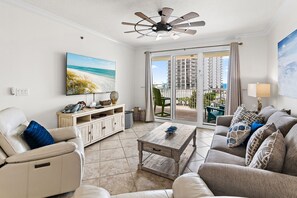 Ein Wohnzimmer mit Sofa, Couchtisch, Fernseher und einem Balkon mit Blick auf das Meer und Gebäude.