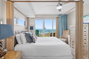 Ein Schlafzimmer mit einem großen Bett, einem Schminktisch, einem Sessel, einem Deckenventilator und einem Balkon mit Blick auf den Strand.
