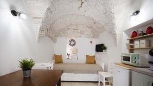 Un espace de vie compact dot é d’un plafond en pierre, d’un canapé, d’une table à manger agrémentée d’une plante, d’un four à micro-ondes et d’un petit coin cuisine.