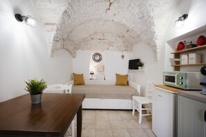 A compact living space with a stone ceiling, a sofa, a dining table with a plant, a microwave, and a small kitchen area. - Cozy apartment on two levels that accommodate up to 3 people and is equipped with all the main comforts for a pleasant stay. The location is excellent, in the center, with all the essential services at hand and a short distance from the points of interes (Martina Franca)