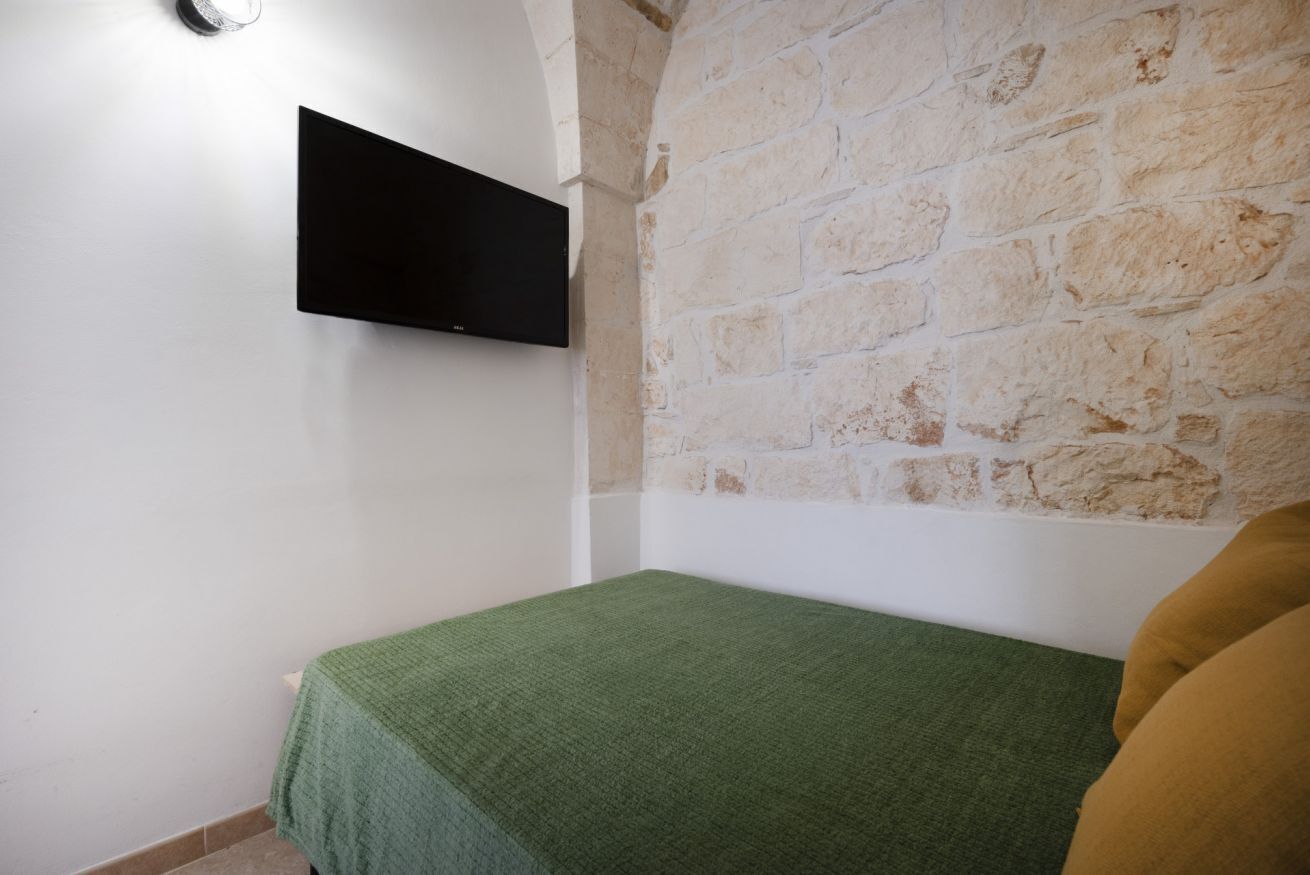 Une chambre avec un lit, un téléviseur à écran plat fixé au mur et un mur en pierre.