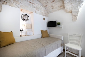 A bedroom with a bed, a chair, a television, a clock, and a shelf with a plant. - Cozy apartment on two levels that accommodate up to 3 people and is equipped with all the main comforts for a pleasant stay. The location is excellent, in the center, with all the essential services at hand and a short distance from the points of interes (Martina Franca)
