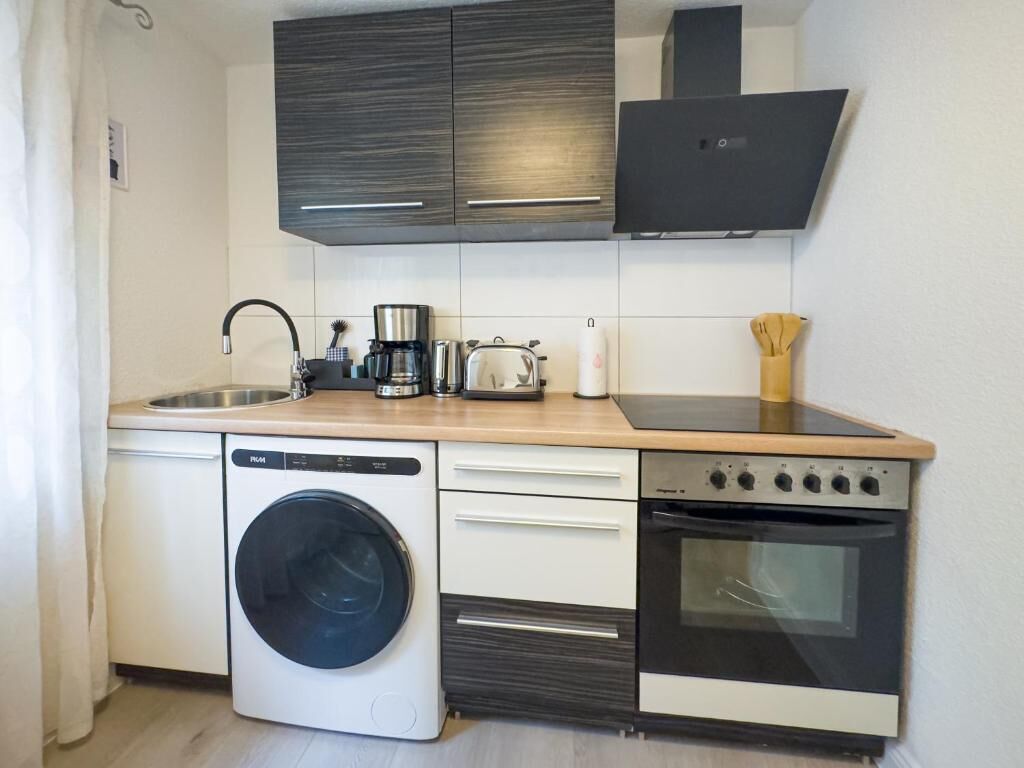 A compact kitchen with a washing machine, a coffee maker, a toaster, and an oven.