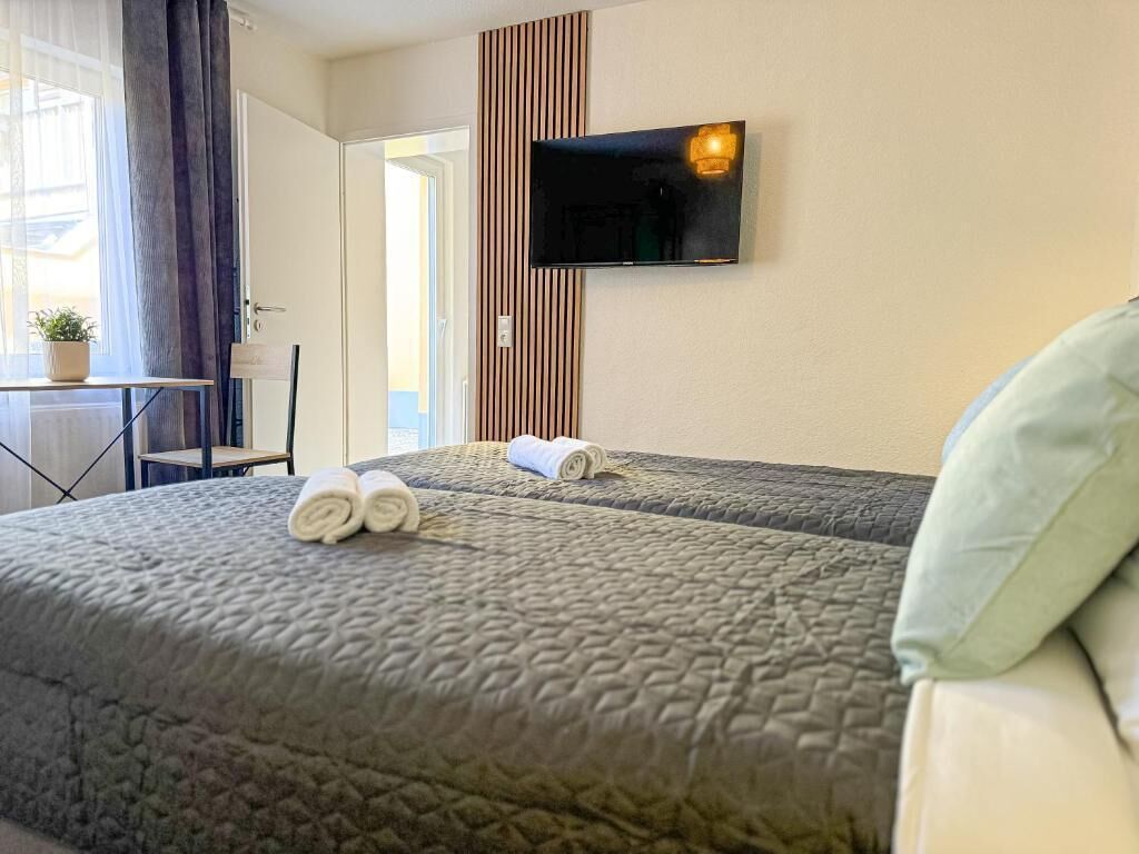 Habitación de hotel con dos camas, un televisor montado en la pared, un escritorio con una silla y una ventana con cortinas.