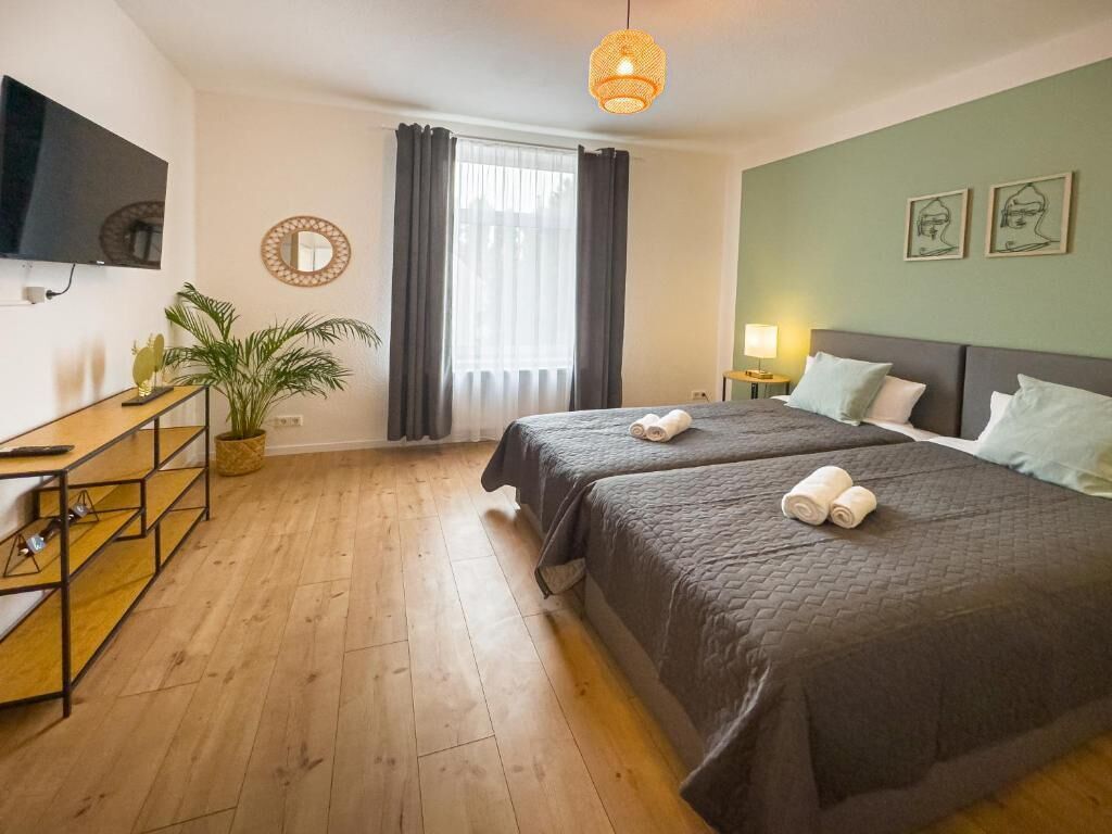Ein Hotelzimmer mit Bett, Schreibtisch, Fernseher, einer Pflanze und einem fenster mit Vorhängen.