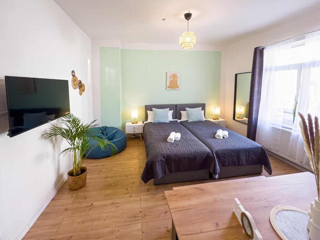 Et hotelværelse med to senge, et fjernsyn, et natbord, en potteplante og et stort vindue.