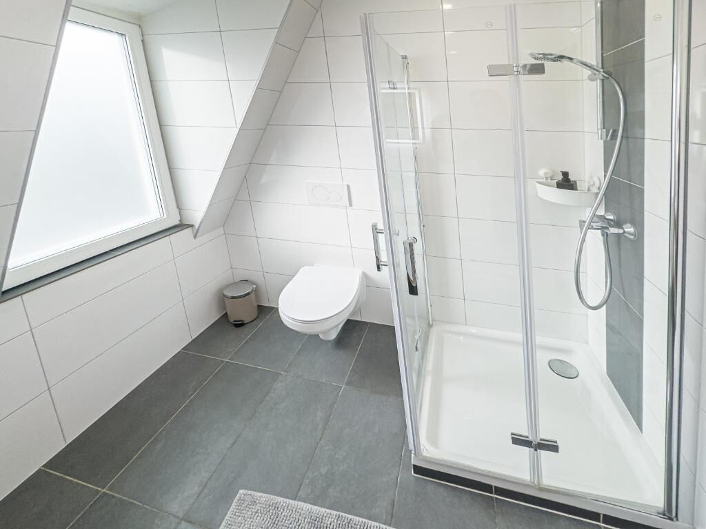 Ein modernes Badezimmer mit einer Duschkabine aus Glas, einer Toilette und einem Fenster.
