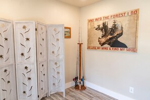 Ein Zimmer mit weißer Wand, einem gerahmten Poster, Holzboden und einem Satz Angelruten.