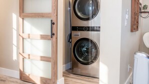 A laundry room with two front-loading washing machines, a wooden sliding door, and a white ceiling fan.