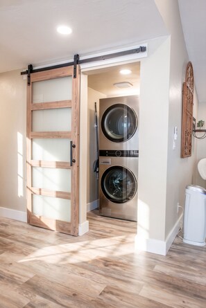 A laundry room with two front-loading washing machines, a wooden sliding door, and a white ceiling fan.