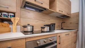 A modern kitchen with wooden cabinetry, stainless steel appliances, and a built-in oven. - Suite Mas de Le Mole (Falcade)
