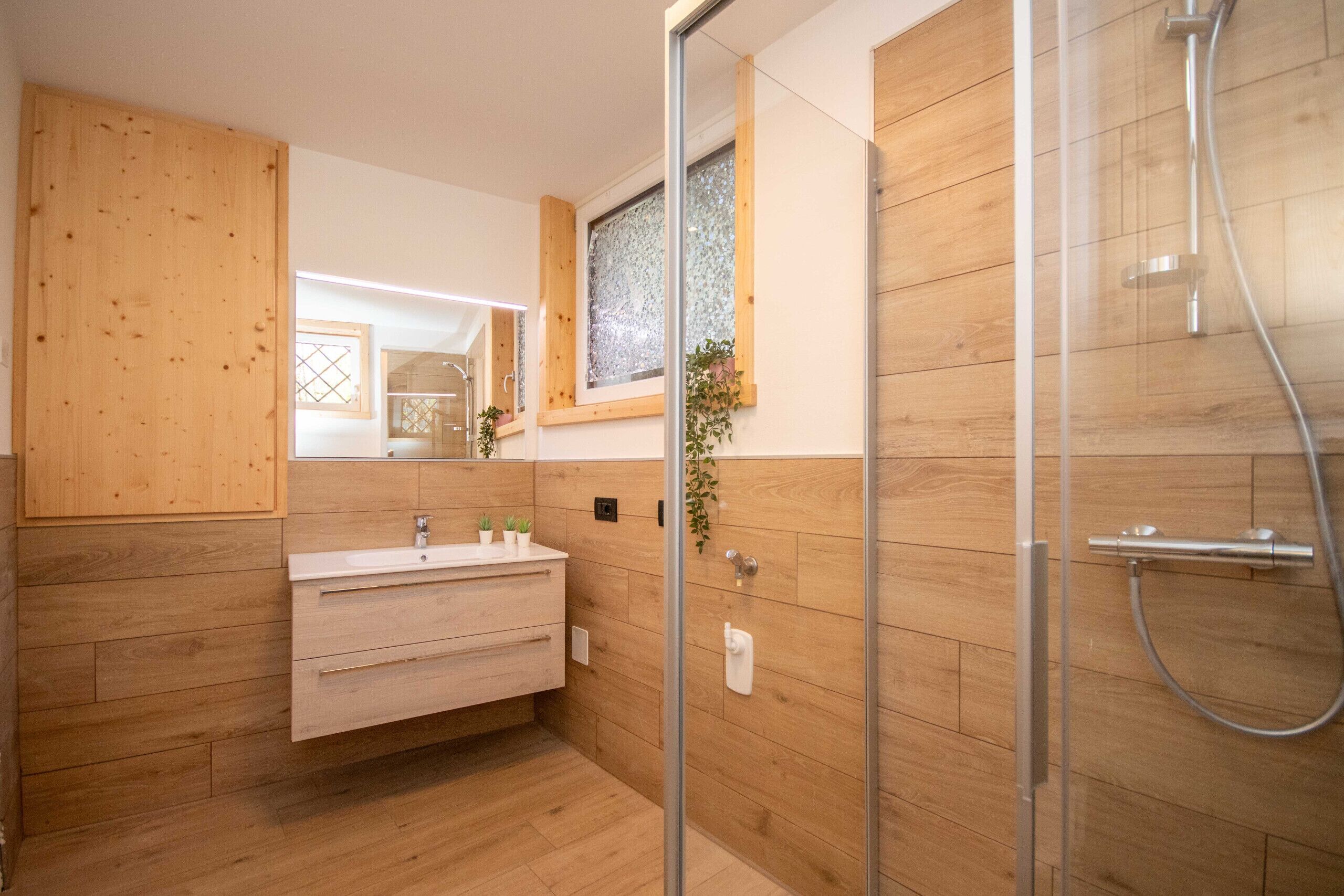 Ein modernes Badezimmer mit Holzvertäfelung, einer Duschkabine aus Glas und einem Waschtisch mit Spiegel.