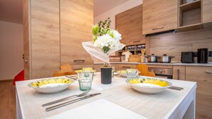 A modern kitchen with wooden cabinets, a dining table set with bowls, glasses, and cutlery. - Suite Mas de Le Mole (Falcade)