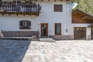 A building with a stone facade, a wooden balcony, a satellite dish, and a paved courtyard.