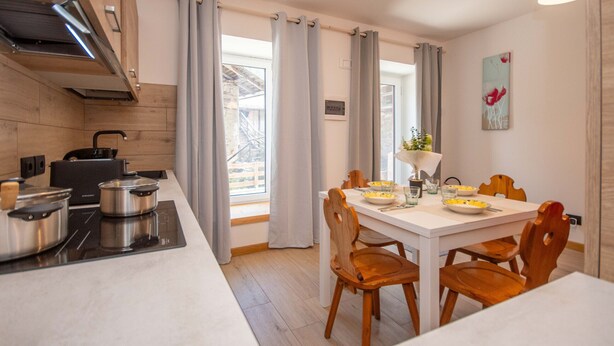 A modern kitchen with a dining area, wooden cabinets, a built-in stove, and a view through large windows. - Suite Mas de Le Mole (Falcade)