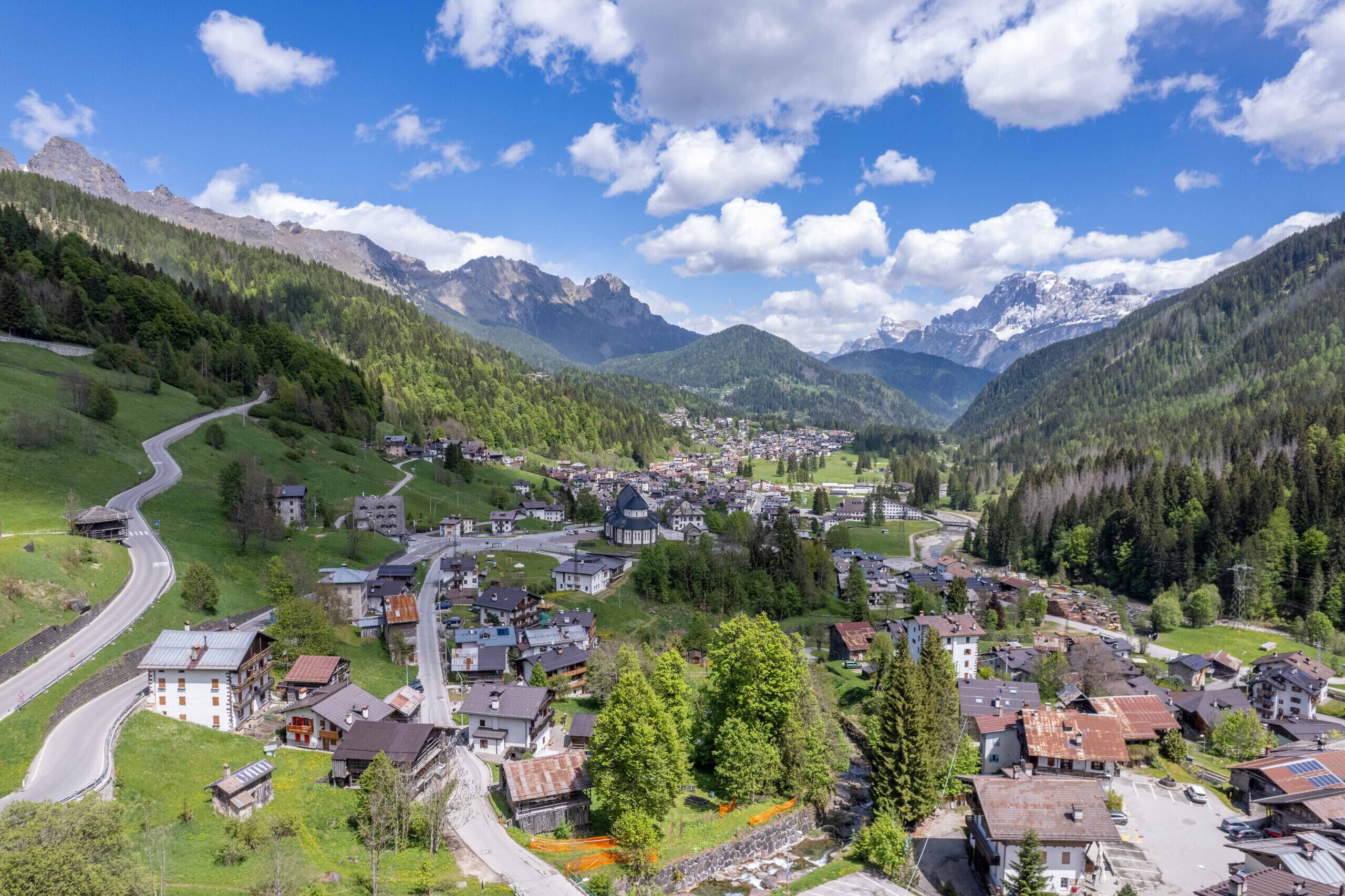 Eine Stadt eingebettet in ein Tal, mit einer kurvenreichen Straße, umgeben von Bergen und dichten Wäldern.