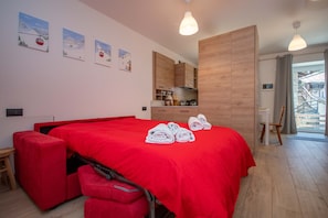 A modern hotel room with a red bed, wooden cabinets, a kitchenette, and a balcony with a view.