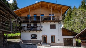A two-story wooden building with a balcony, a stone-paved courtyard, and a mountain backdrop. - Suite Mas de Le Mole (Falcade)
