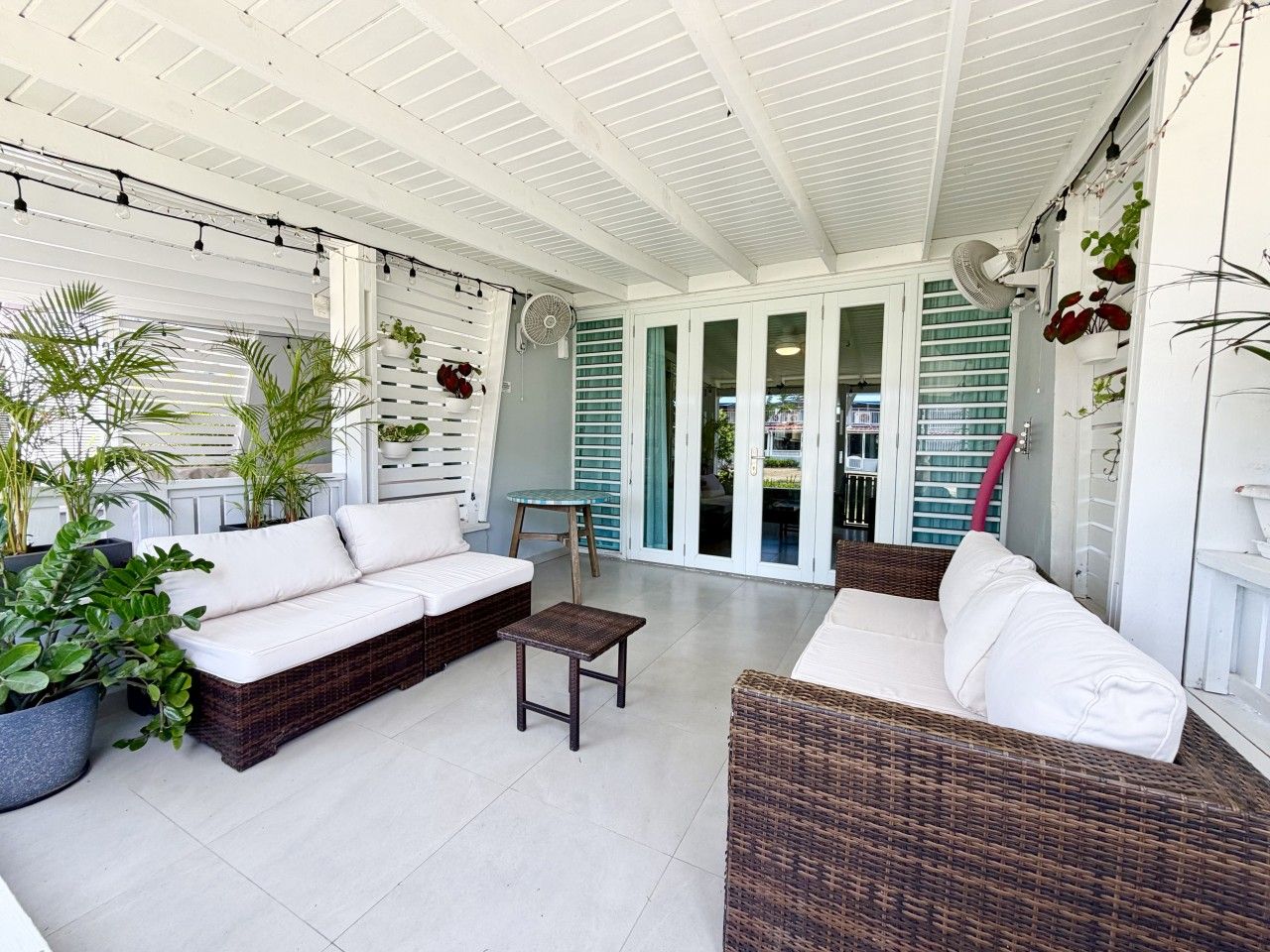 A covered outdoor seating area with wicker furniture, potted plants, and a fan.