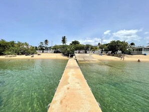 Una playa con aguas cristalinas, un paseo marítimo de concreto y palmeras.