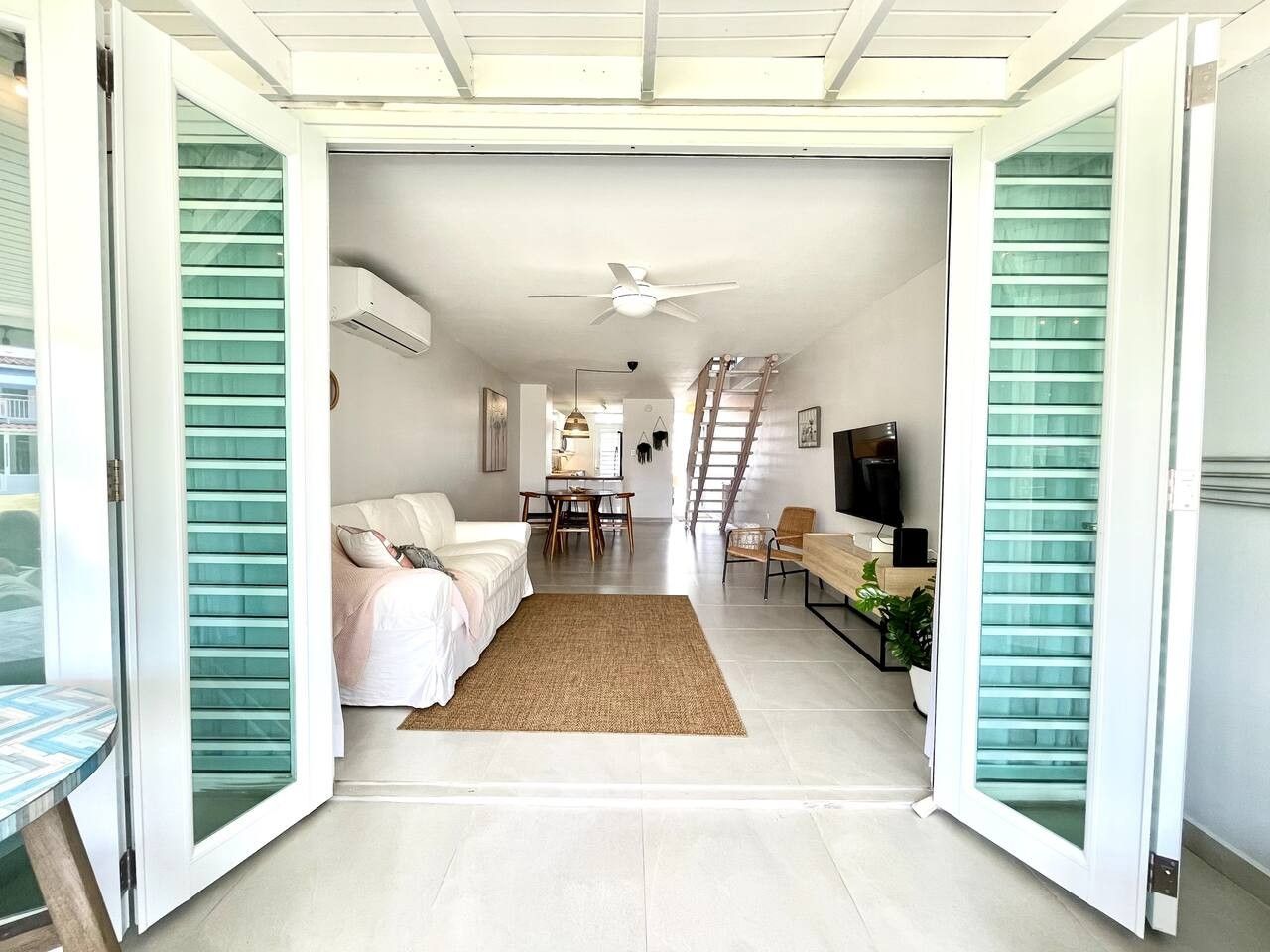 Un espacio habitable abierto con sofá, mesa de comedor, televisor y escalera.