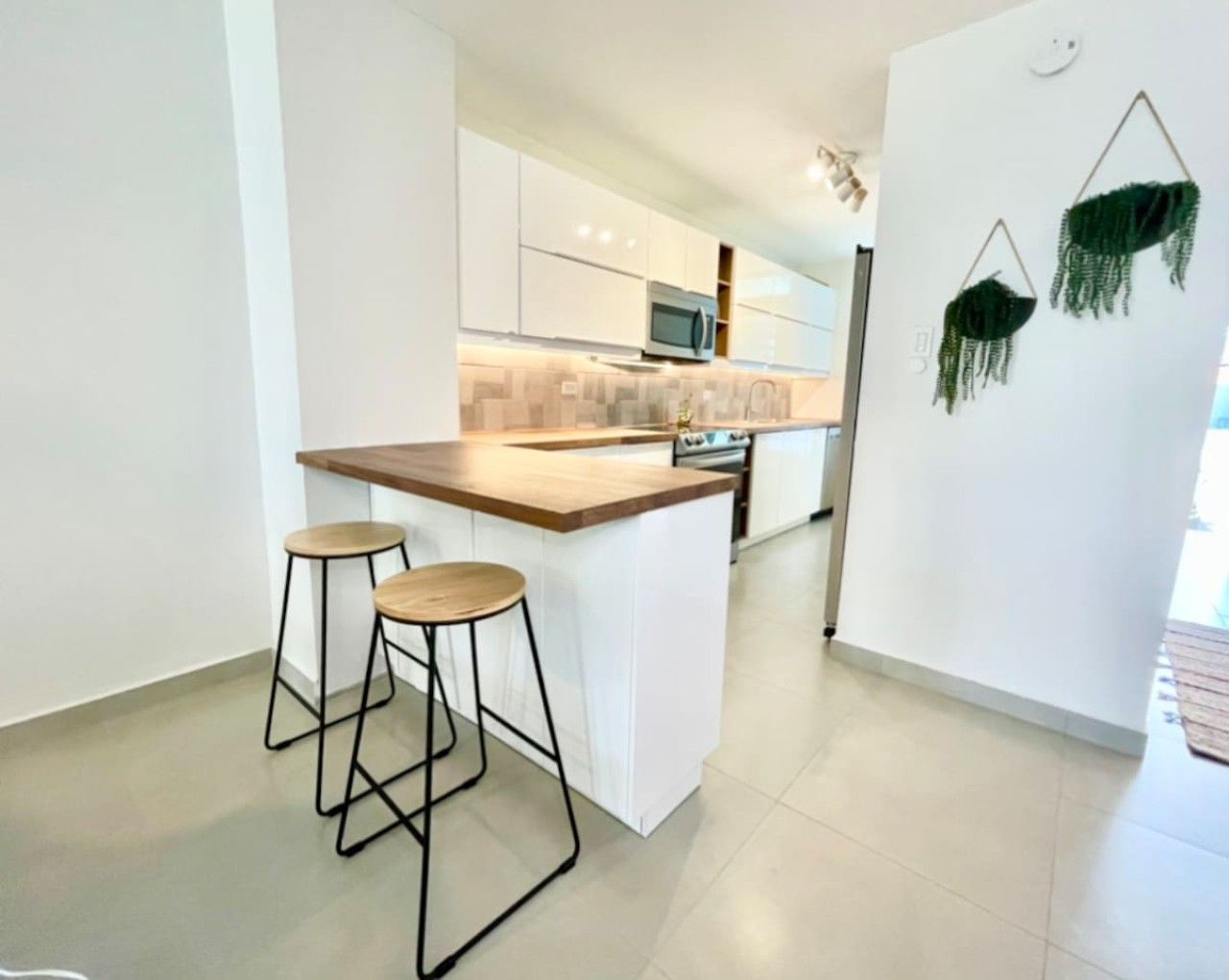 A modern kitchen with white cabinets, a wooden countertop, and two bar stools.