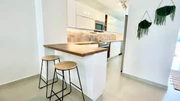 A modern kitchen with white cabinets, a wooden countertop, and two bar stools.
