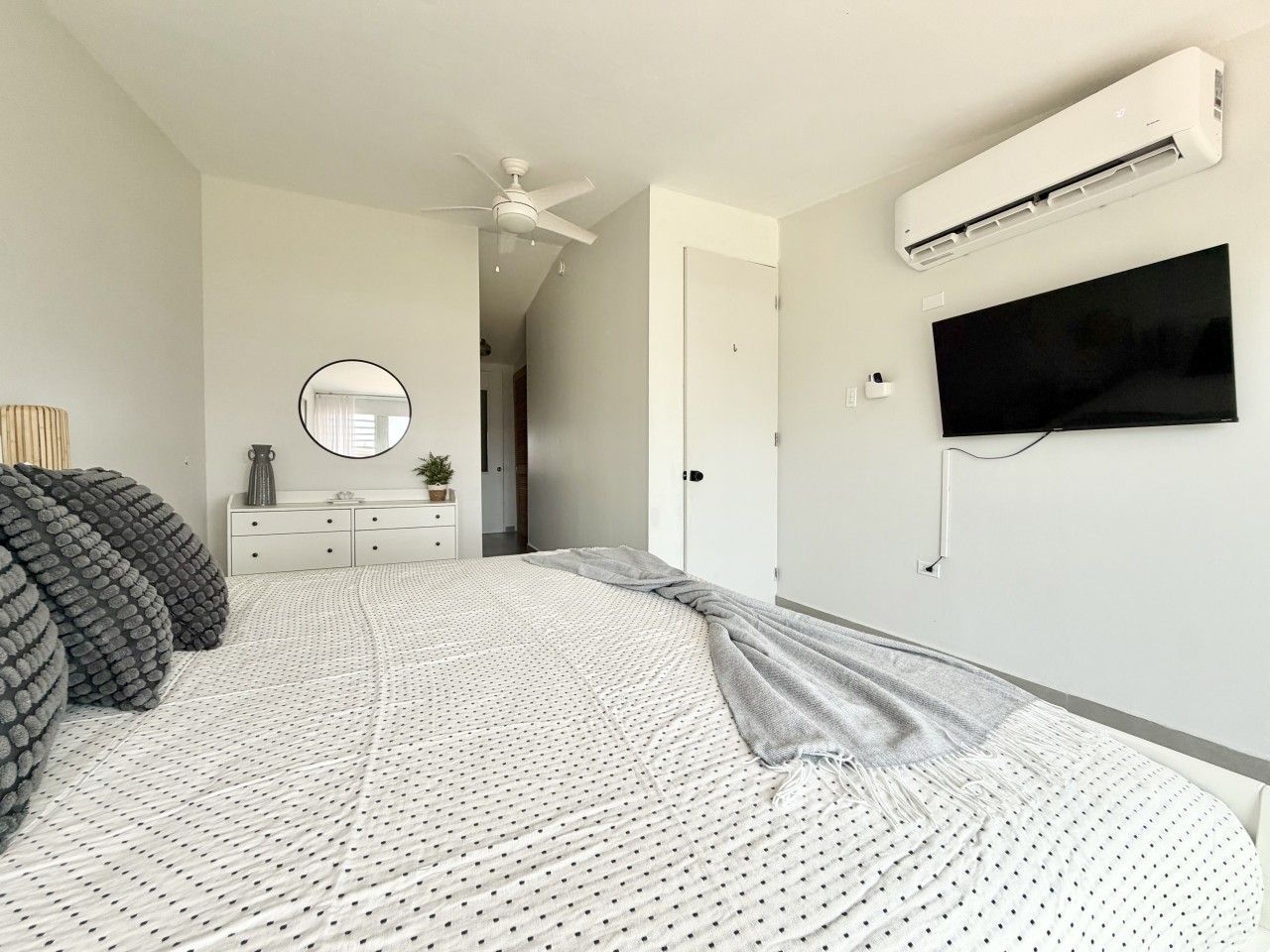 A bedroom with a bed, a dresser, a mirror, an air conditioning unit, and a television.