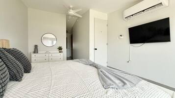A bedroom with a bed, a dresser, a mirror, an air conditioning unit, and a television.