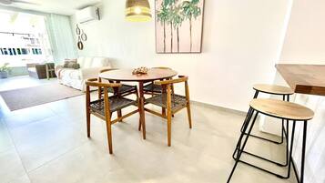 A modern living room with a dining area, a hanging light fixture, and a wall-mounted air conditioner.